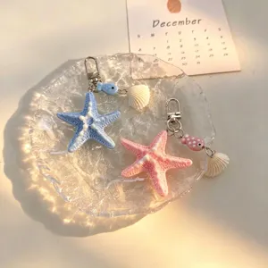 Vue détaillée des porte-clés étoile de mer et coquillage sur un plateau en verre.