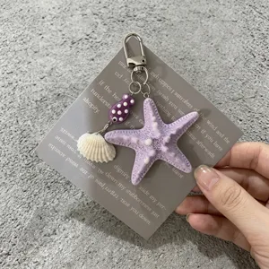 Gros plan d'un porte-clés thème marin avec étoile de mer violette et son coquillage.