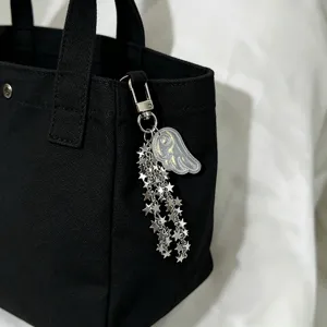 Detail showing an angel wing and silver star chain bag charm on a black tote bag.