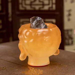Close-up of translucent orange Buddha head resin figurine with crystal stone