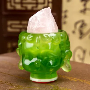 Close-up detail of a decorative green resin Buddha head figurine with a pink quartz rough stone