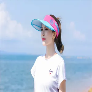 Asiatisches Model trägt eine rosa-blaue Sonnenblende am sonnigen Strand zum Sonnenschutz