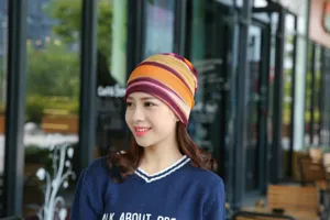 Asiatische Frau trägt eine farbenfroh gestreifte Beanie-Mütze in einem urbanen Viertel.