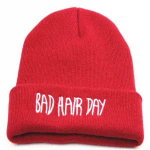 Detaillierte Nahaufnahme der weißen BAD HAIR DAY Stickerei auf einer roten Strickmütze