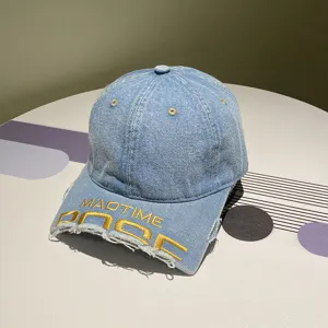 Nahaufnahme einer blauen Denim-Baseballkappe mit gelber MADTIME-Stickerei und Fransen.