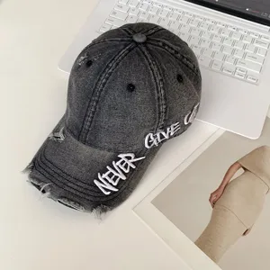 Vista detallada de una gorra de béisbol de mezclilla gris con bordado "NEVER GIVE UP".