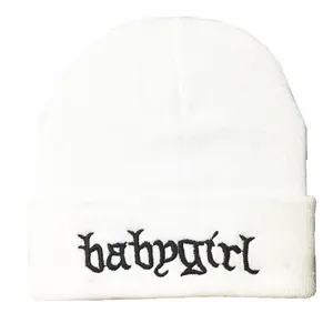 Nahaufnahme der schwarzen 'babygirl' Stickerei auf einer weißen gestrickten Beanie-Mütze