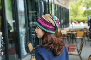 Seitenansicht einer Frau mit einer bunt gestreiften Beanie-Mütze in einem Straßencafé.