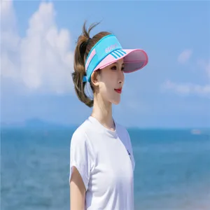 Modell trägt ein blau-pinkes Sonnenvisier am sonnigen Strand vor einem Meereshintergrund.