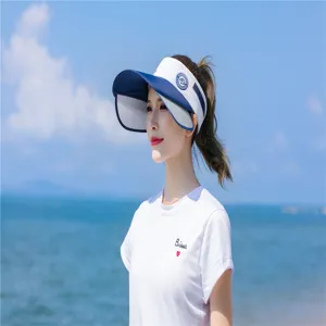 Asiatische Frau mit einem stilvollen blau-weißen Sonnenvisier an einem sonnigen Strand.