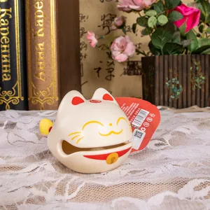 Dettaglio ornamento da scrivania Maneki-neko Muyu su tovaglia di pizzo con libri