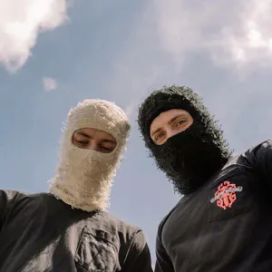 Zwei Models mit zotteligen, abgenutzten Strick-Sturmhauben vor blauem Himmelshintergrund