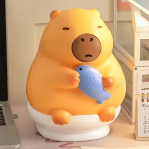 Adorable capybara vinyl piggy bank holding a blue fish on a white toilet base for kids