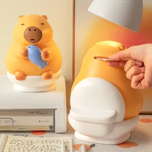 Cute yellow Capybara vinyl piggy bank holding a blue fish sitting on a toilet for kids gift