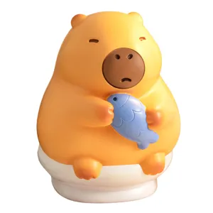 Cute cartoon capybara vinyl piggy bank holding a blue fish, decorative money box kids gift