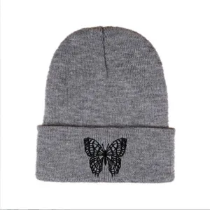 Detailed view showing the black butterfly embroidery on the cuff of a grey knitted beanie