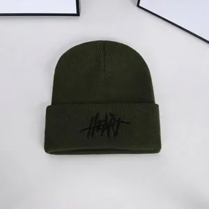 Detailed macro view of a dark green knitted beanie hat with black Heart embroidery