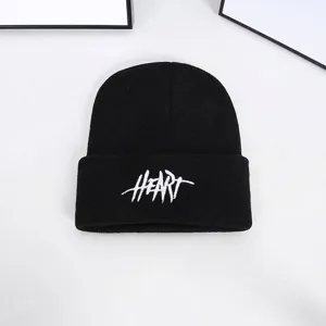High-quality close-up of a black knitted beanie featuring white HEART embroidery detail