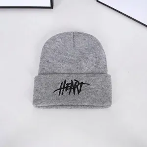 Detailed close-up of a grey knitted winter beanie hat with bold black 'HEART' embroidery.
