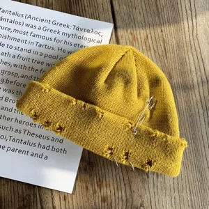 Detail van een gele gebreide muts met distressed randen, een veiligheidsspeld en ringen.