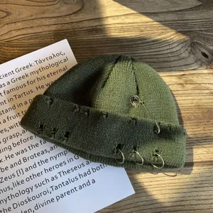 Detailweergave van donkergroene gebreide muts met zilveren ringen en een speld