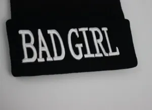 Détail du texte brodé en 3D BAD GIRL sur un bonnet en tricot noir unisexe.
