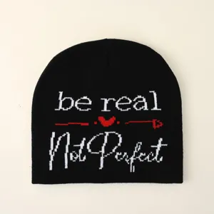 Dettaglio del testo lavorato a maglia 'be real Not Perfect' sul berretto nero