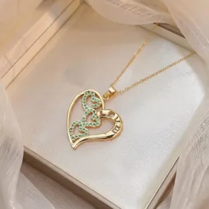 Dettaglio macro della collana con ciondolo a cuore dorato, pietre verdi e incisione LOVE