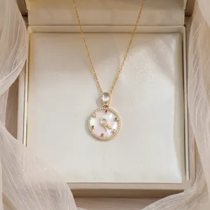 Detail of golden necklace with mother of pearl pendant and colorful zircon accents.