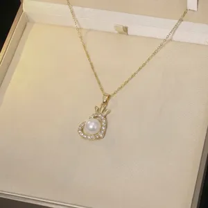 Close-up of heart-shaped gold necklace with pearl and crystal crown pendant in gift box.