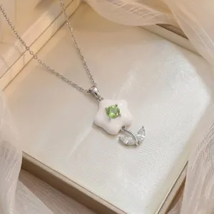 Détail d'un élégant pendentif fleur avec zircon vert et pétales en émail blanc brillant.