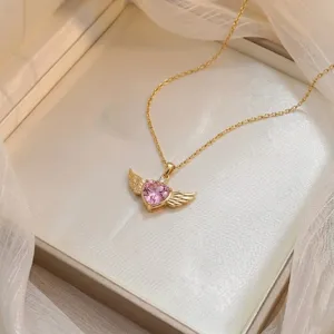 Primer plano de un collar de alas de ángel de oro con colgante de corazón de circón rosa.