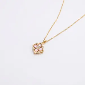 Gros plan du collier avec pendentif doré, pierre rose à quatre pétales et centre zircon.