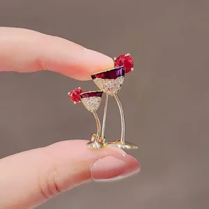 Detailed close-up of elegant wine glass brooch with red gemstones and gold finish plating