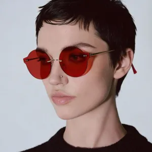 Detail view of a model wearing rimless round sunglasses with vibrant red candy-colored lenses.