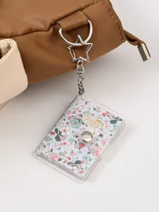 Detailed close-up shot of a clear PVC mini notebook keychain with floral cover attached to a bag.