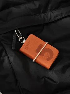 Close-up detail of mini leather notebook keychain with number five design on black bag.