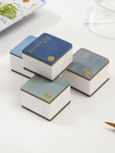Gedetailleerd overzicht van vierkante draagbare aquarellosjes met gestructureerde kaft en goudfolie.