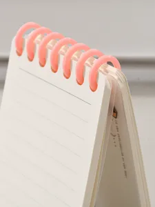 Gros plan détail du carnet à spirale de poche A7 avec anneaux en plastique rose et pages lignées.