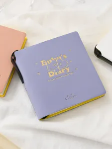Detalle de cuaderno de bolsillo violeta con texto de gato en lámina dorada y bolígrafo