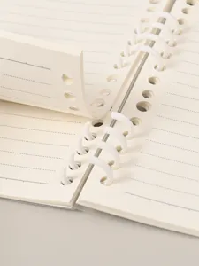 Detailopname van crème notitieboekje met gescheiden witte plastic ringen en gelinieerde pagina's.