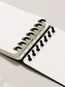 Detail view of a discbound notebook with black plastic rings and neat lined pages.
