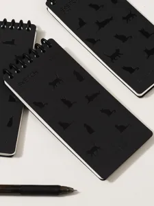 Close-up detail of black spiral mini notebook with cute cat silhouettes and elastic band design.