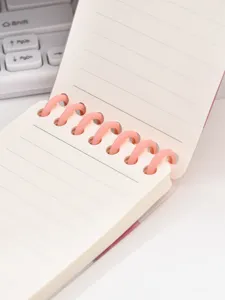 Detalle de mini cuaderno de espiral con anillas rosas de plástico y papel rayado de bolsillo.