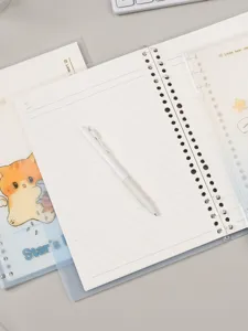 Vista detallada de cuaderno de hojas sueltas B5 con páginas rayadas, dibujo de gato y bolígrafo.