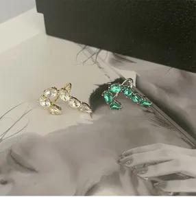 Detail view of French-style J-shaped stud earrings with white and green zirconia crystals
