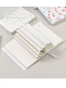 Vista detallada del cuaderno floral estético con cubierta transparente y páginas creativas enrolladas.