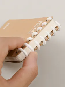 Detailopname van A7 zakformaat ringbandnotitieboekje met witte plastic ringen en gelinieerd.