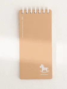 Gros plan d'un carnet a spirale marron avec reliure blanche et motif de cheval a bascule.