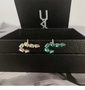 Close-up of J-shaped earrings with clear and green zirconia on a black jewelry box
